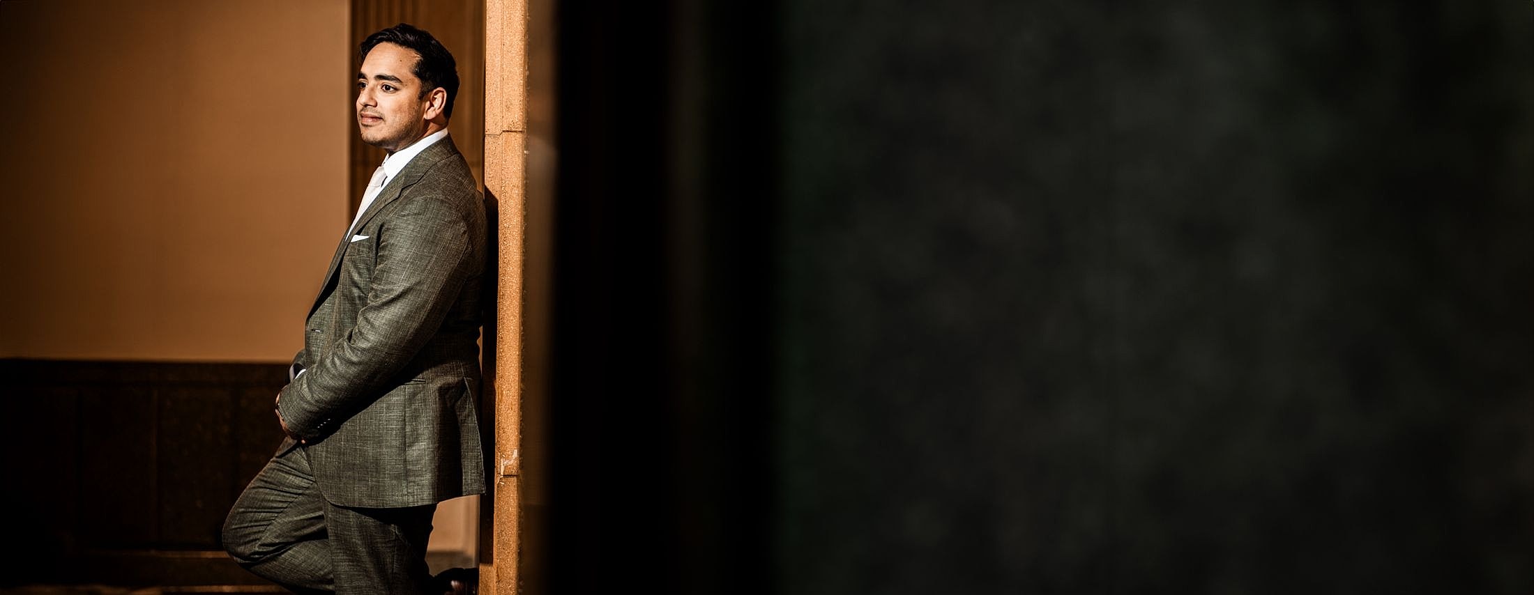 Elk Grove Village plastic surgeon, Dr. Sameer Kapadia, in a stylish suit leaning against wall.