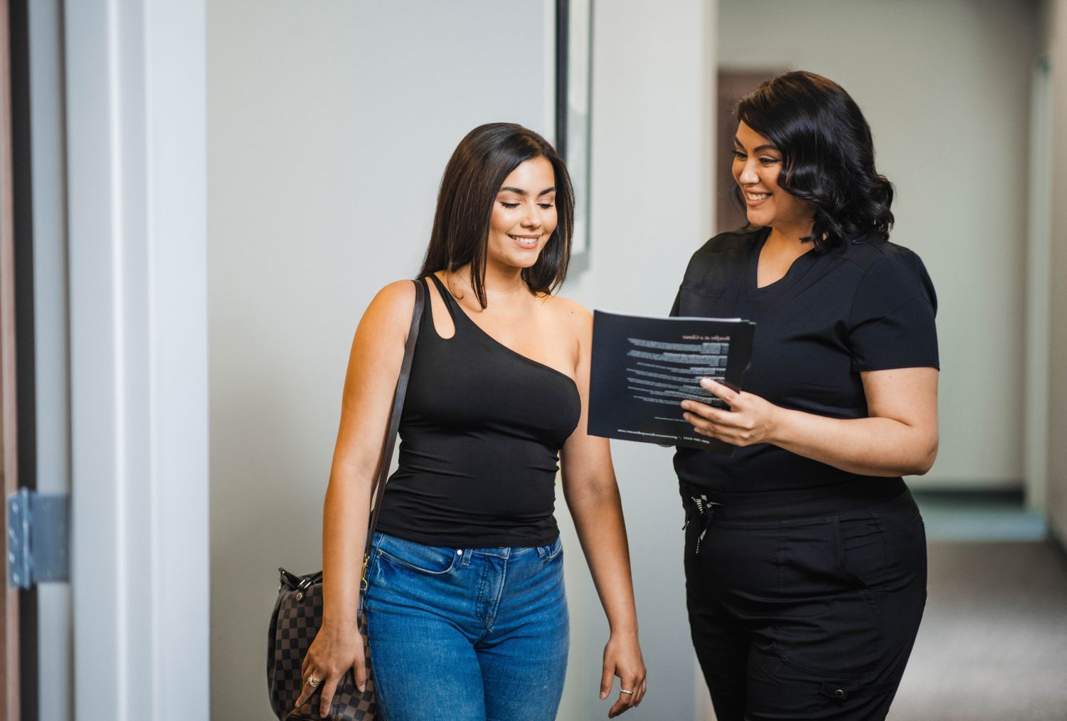 Women discussing in a hallway, holding documents.