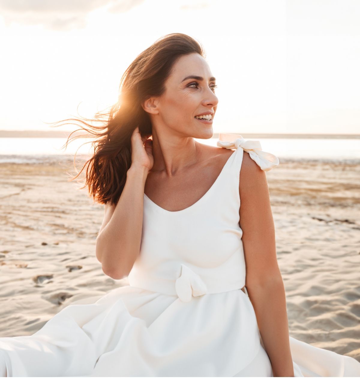 Woman in white dress by the beach at sunset.