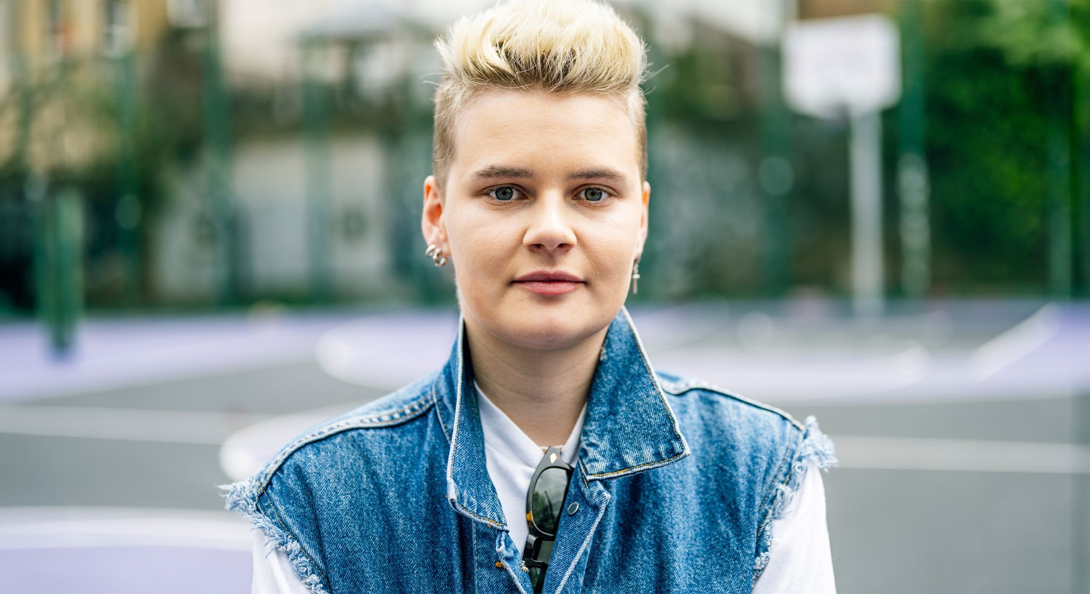 Person with short hair and denim jacket outdoors.