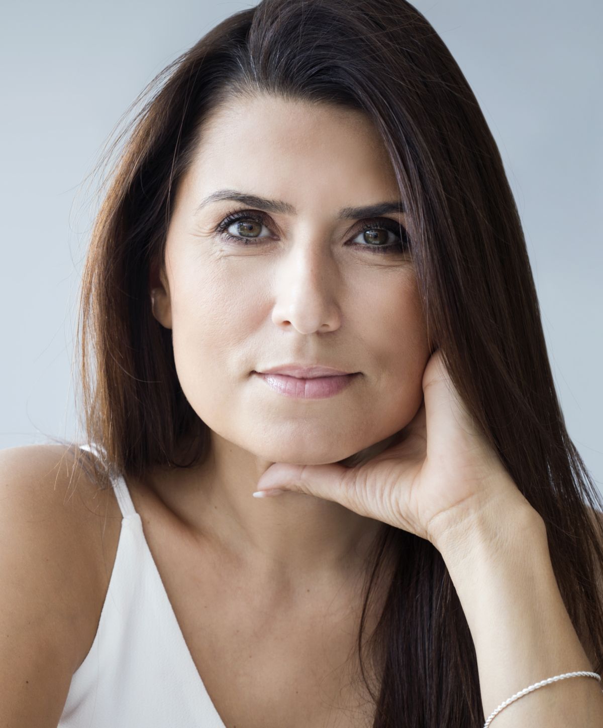 Woman with long hair resting chin on hand.